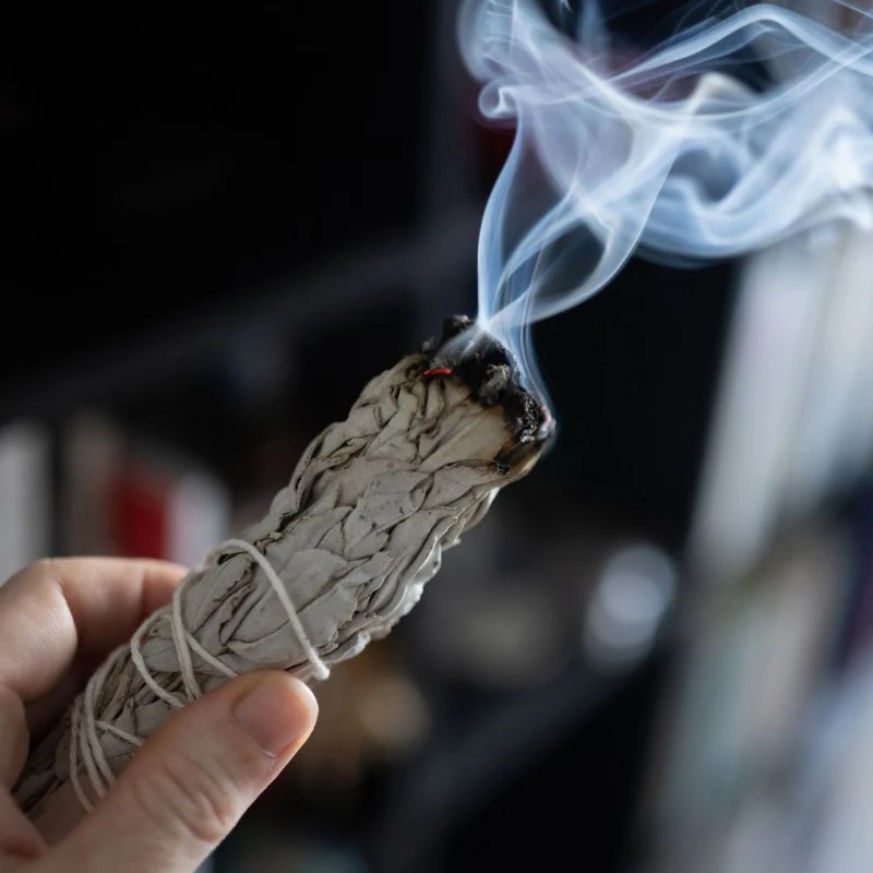 Smoldering white sage bundle with smoke over a ceramic plate, in use